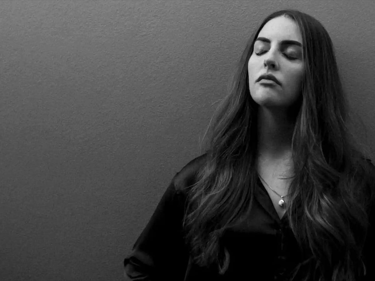 Composer Natalie Nicolas poses with her eyes closed against a dark backdrop.