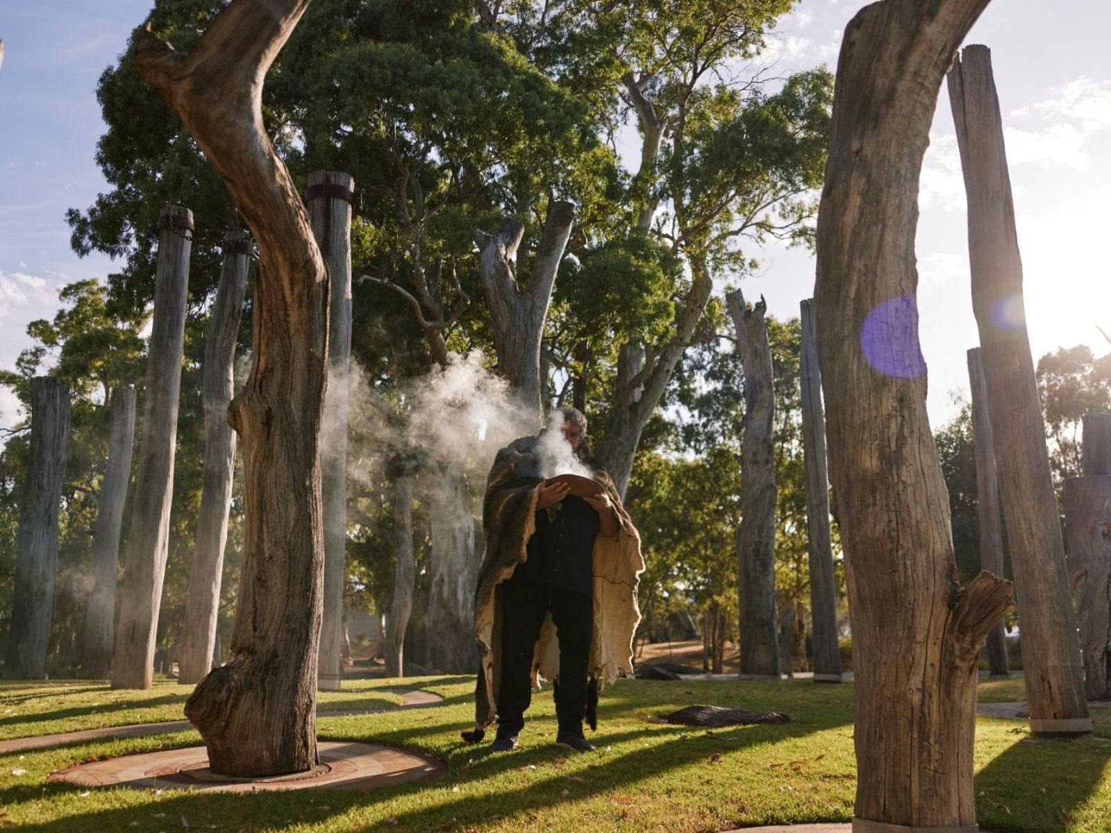 A man wearing a possum skin cloak performing a smoking ceremony