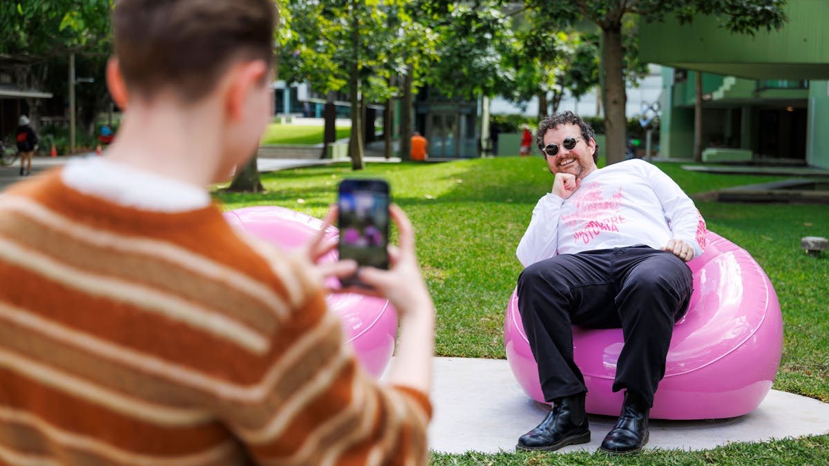 Man posing for a photo on a solid pink chair that looks like its inflatable