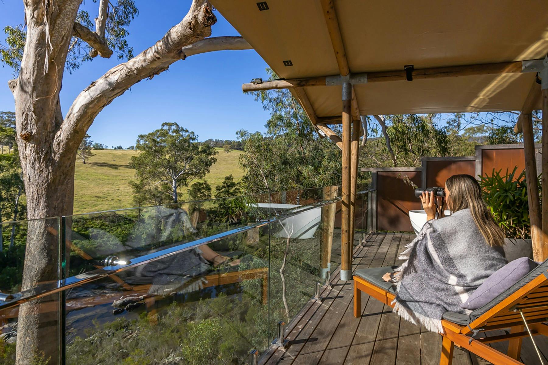 ベランダに座って双眼鏡で下の川を眺める女性