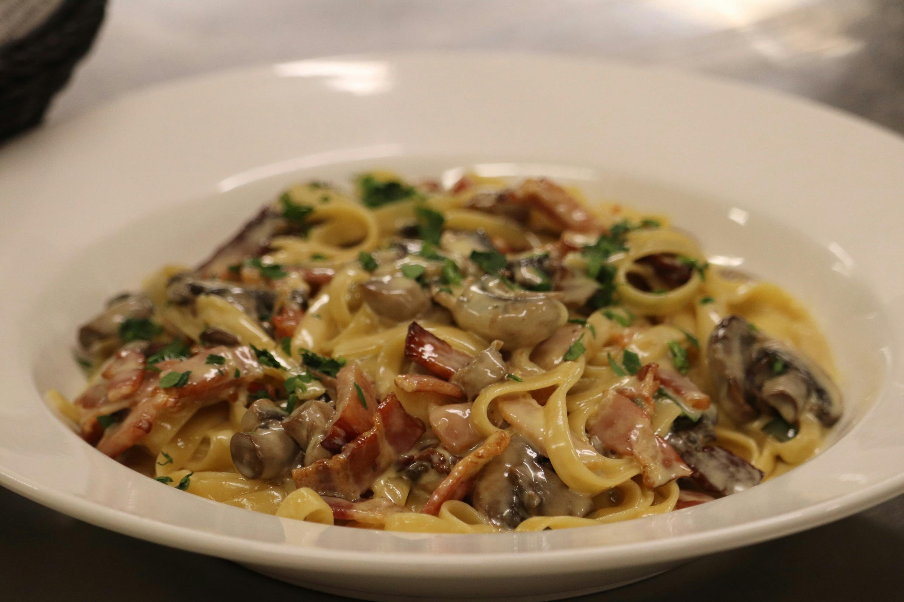 Creamy pasta with mushrooms and bacon, garnished with herbs in a white bowl.