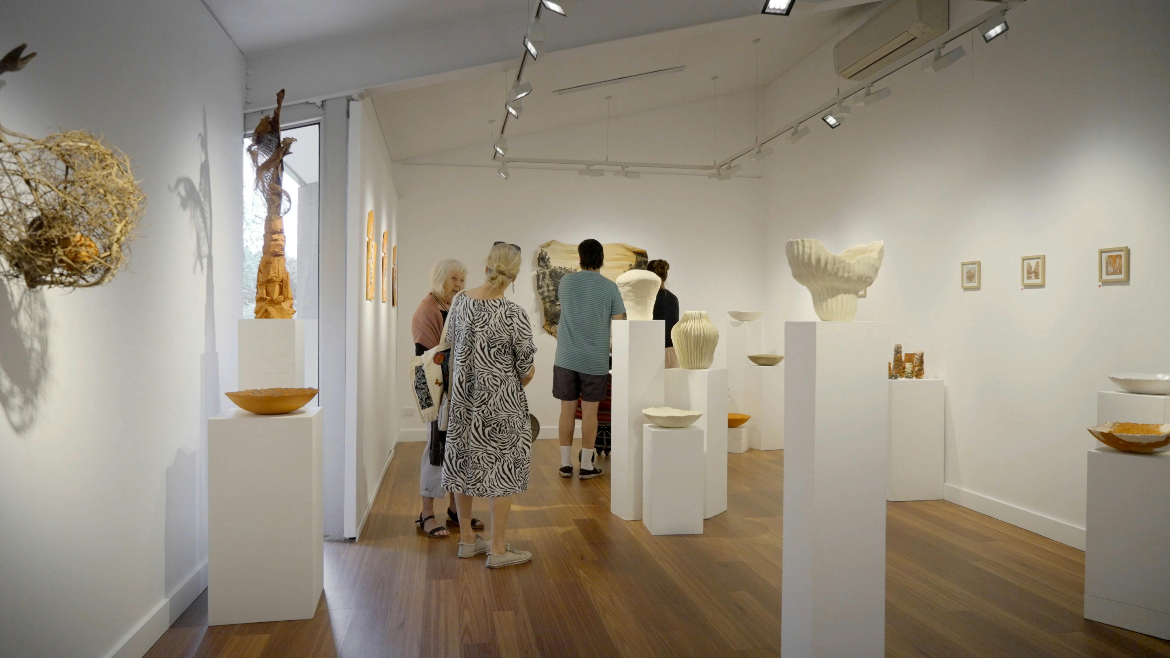 Photograph of people in a small gallery space among various ceramic artworks.