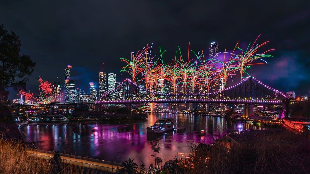 Bright orange and green fireworks explode from the Story Bridge