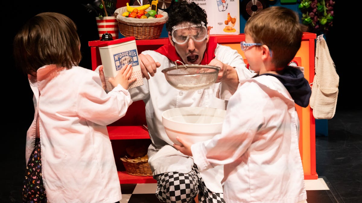 A person in goggles, holding a sieve over a mixing bowl, looks surprised in a playful kitchen scene A person in goggles, holding a sieve over a mixing bowl, looks surprised in a playful kitchen scene