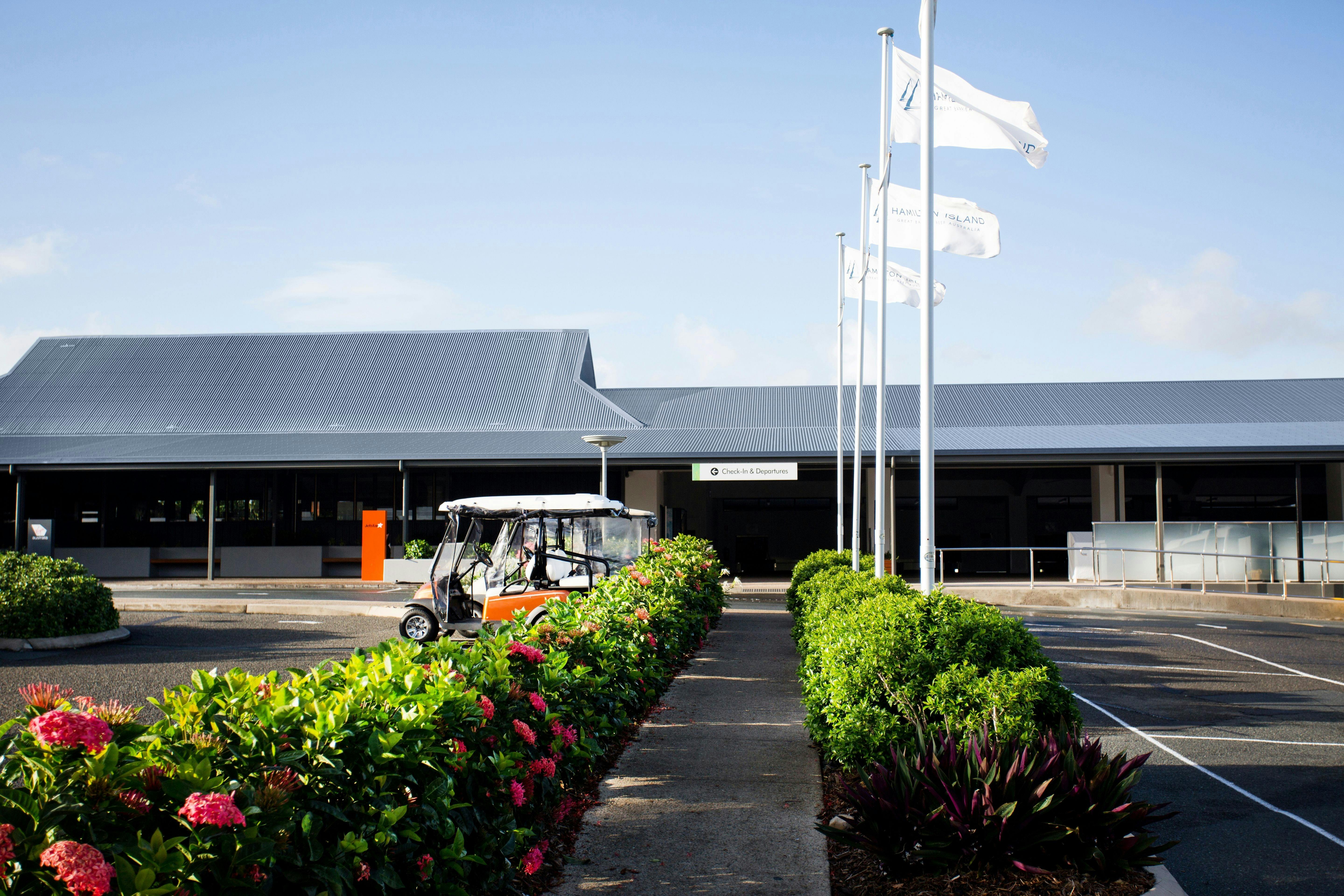 outside view to a small airport building with green bushes along the footpath
