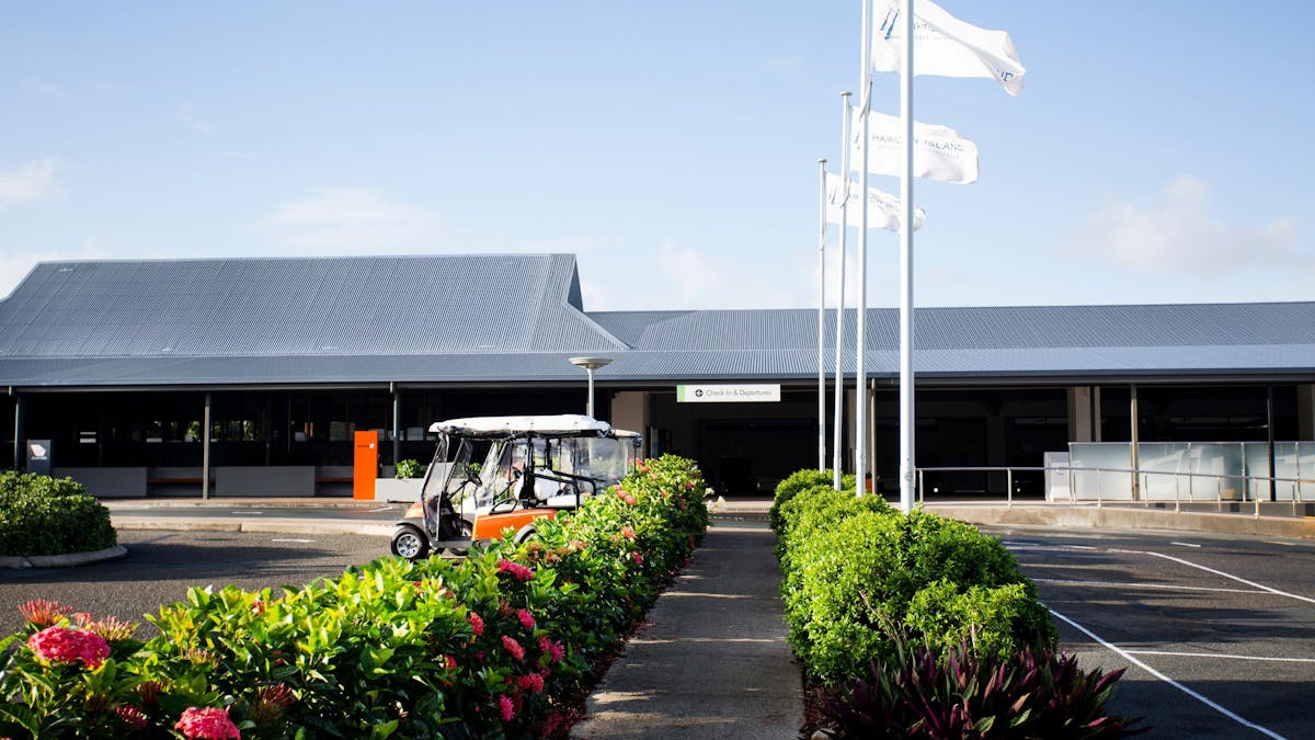 outside view to a small airport building with green bushes along the footpath