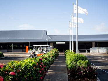 outside view to a small airport building with green bushes along the footpath