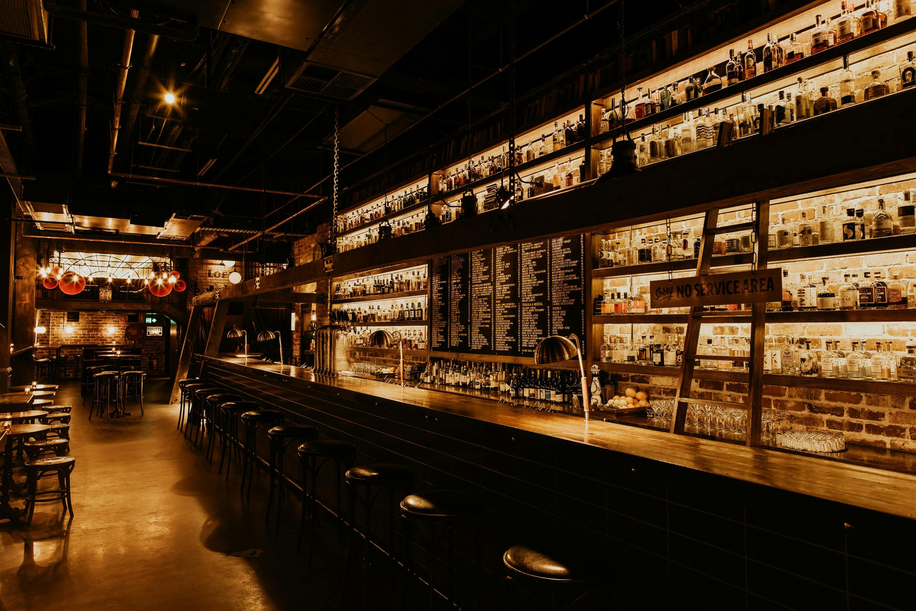 Low Lit bar with high shevles is pictured with spirits on the shelves