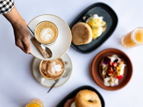 A table set with breakfast dishes with a cup on coffee in hand over the top of the meals