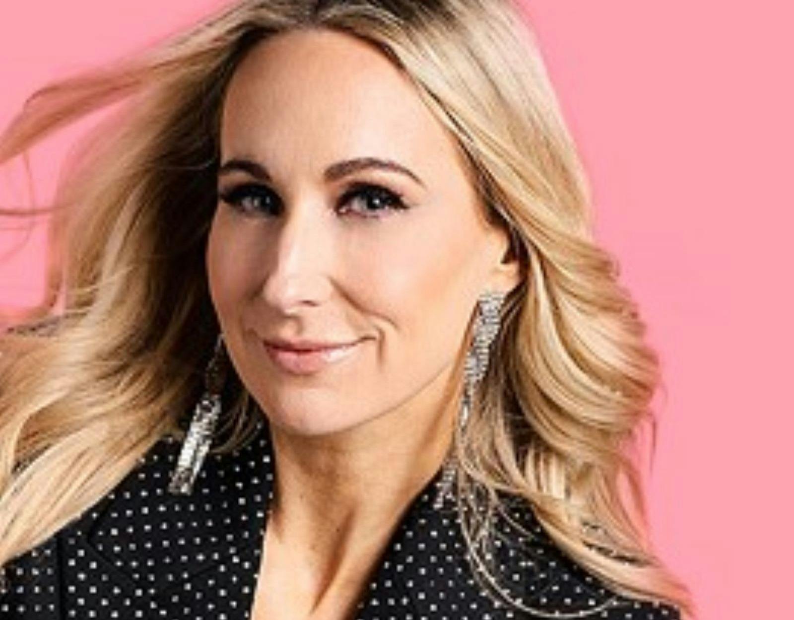 A photo of Nikki in front of a light pink background smiling.