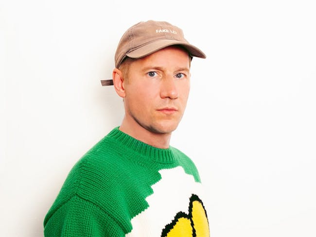 DJ / Producer Riton Wearing a green jumper and brown cap looking directly at camera