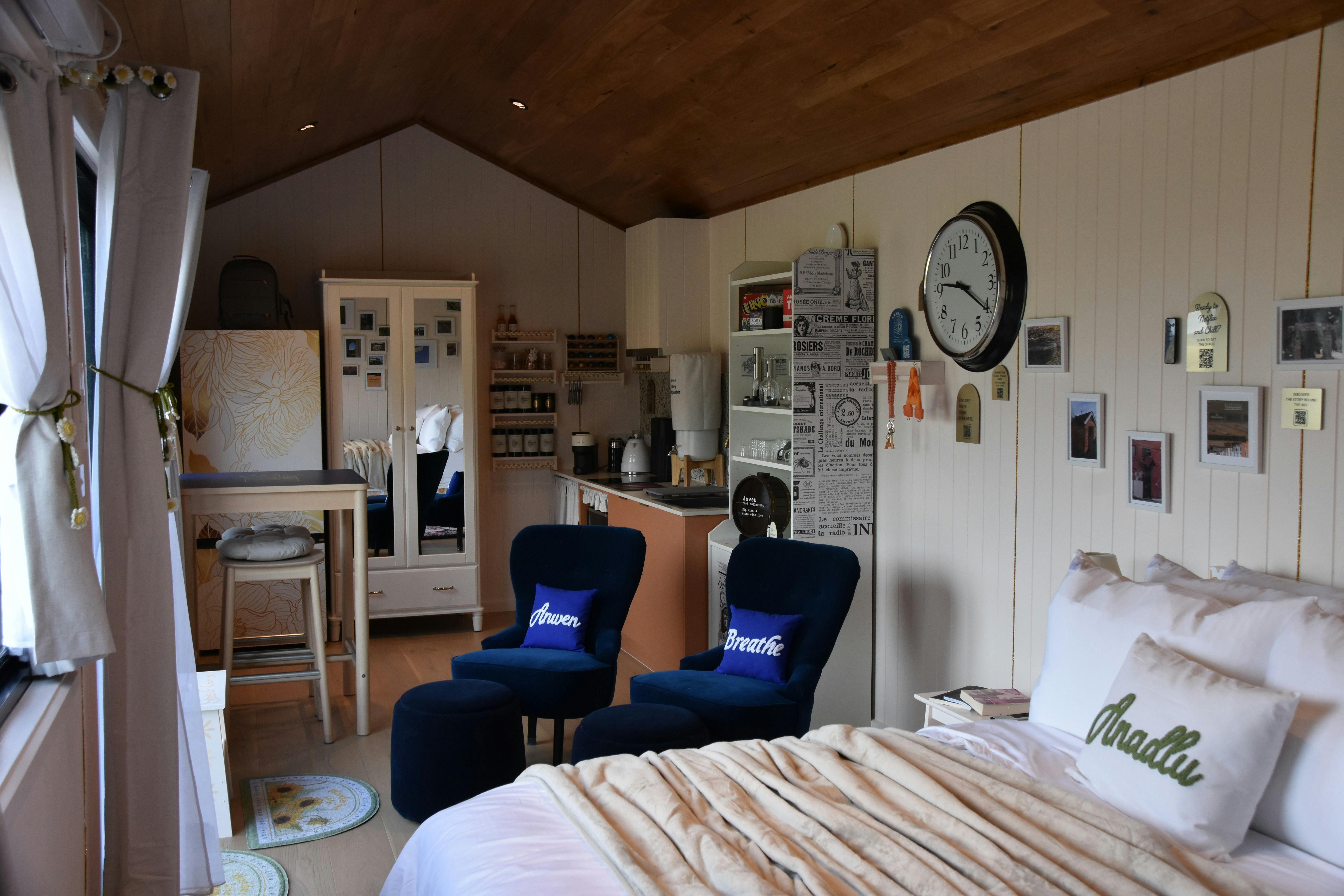 Interior of Anwen tiny home showing bed, lounge chairs, kitchenette and warm timber ceiling