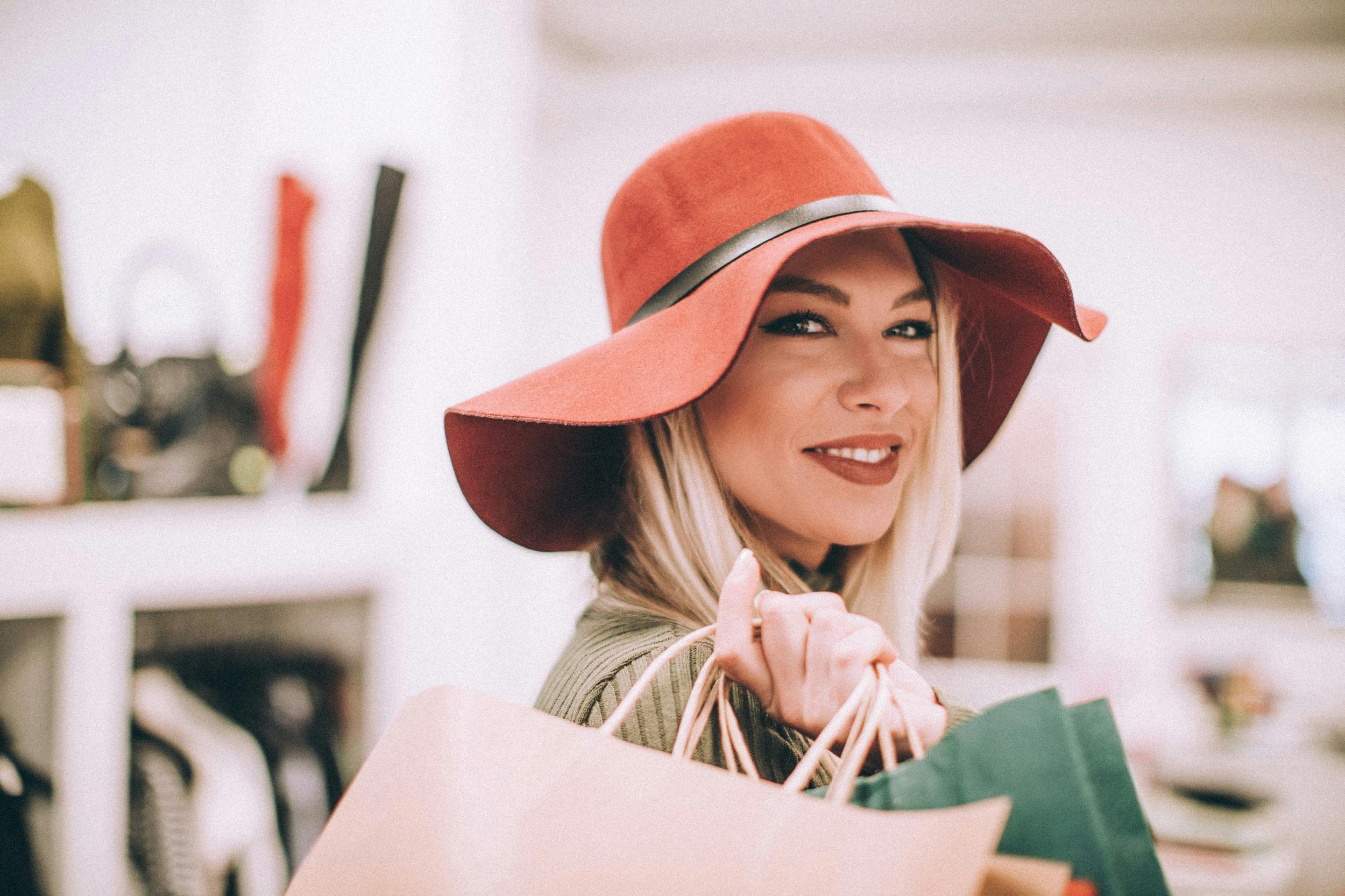 A woman wearing a wide-brimmed hat with a handbag over her shoulder smiling at the camera