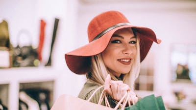 A woman wearing a wide-brimmed hat with a handbag over her shoulder smiling at the camera