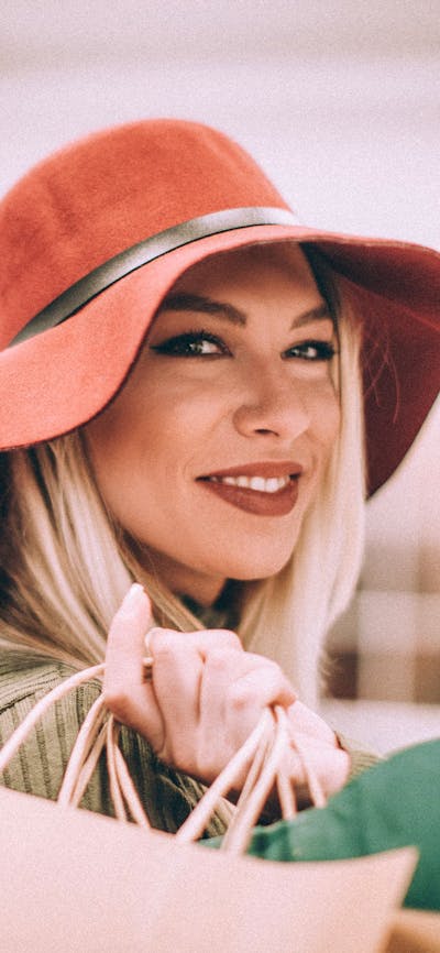 A woman wearing a wide-brimmed hat with a handbag over her shoulder smiling at the camera
