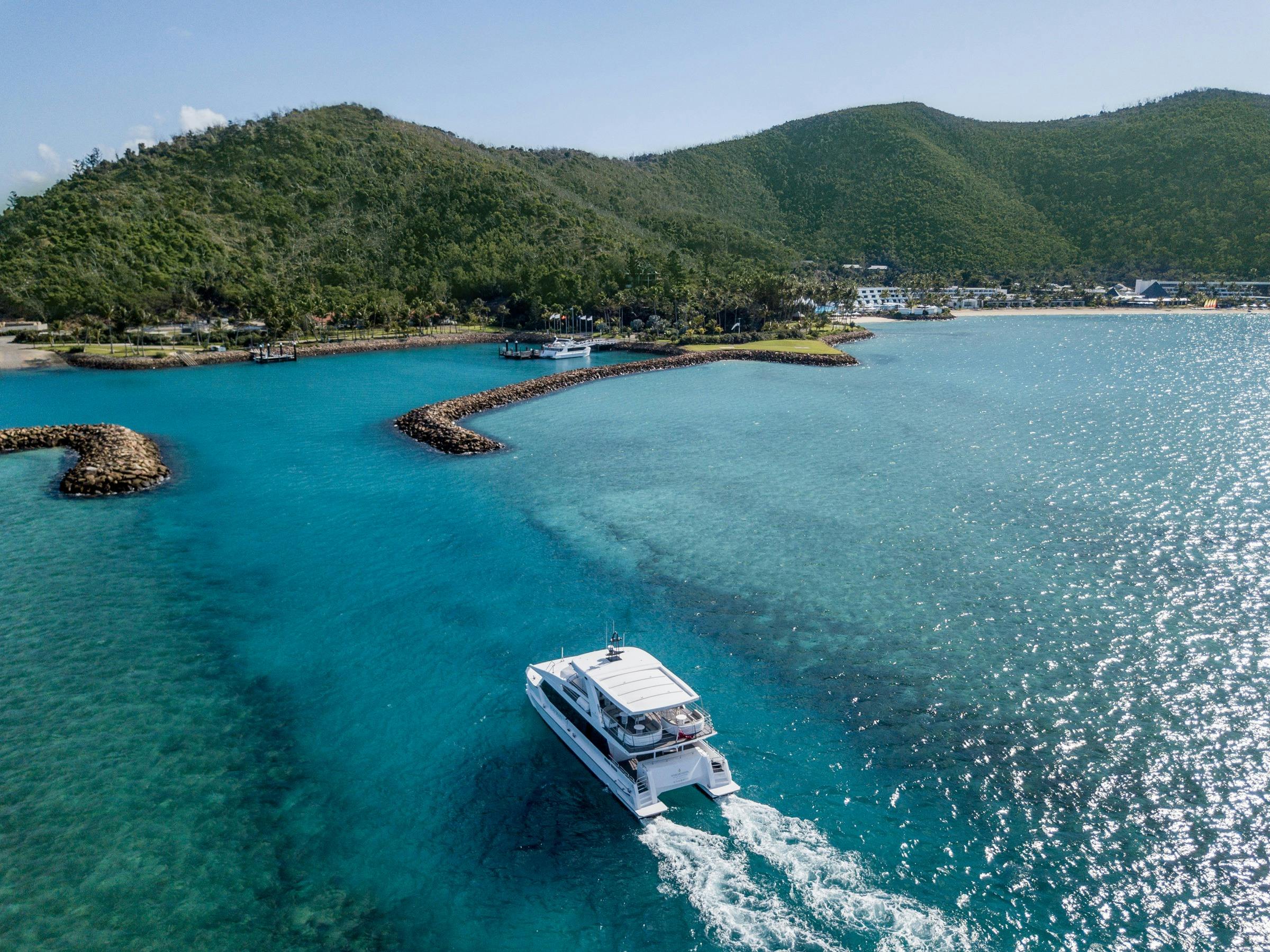 A luxury boat approaches Hayman Island, surrounded by turquoise waters and lush green hills.