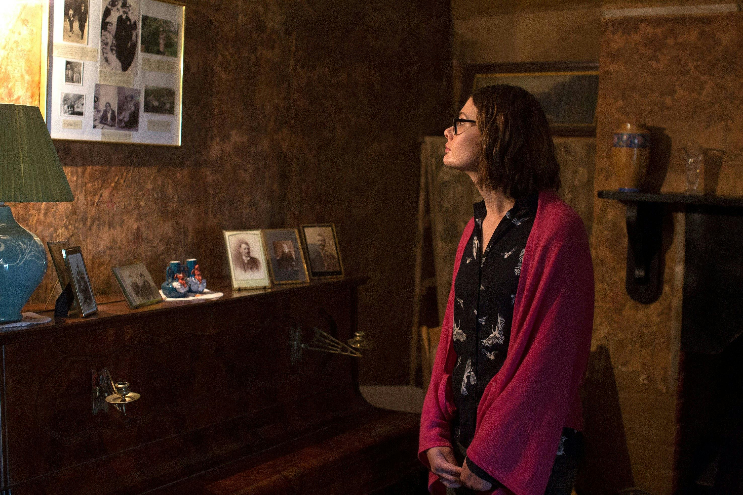 Dark living room at Mugga depicting lady lookin at old photos in wall and piano top