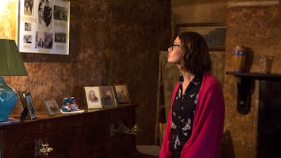 Dark living room at Mugga depicting lady lookin at old photos in wall and piano top