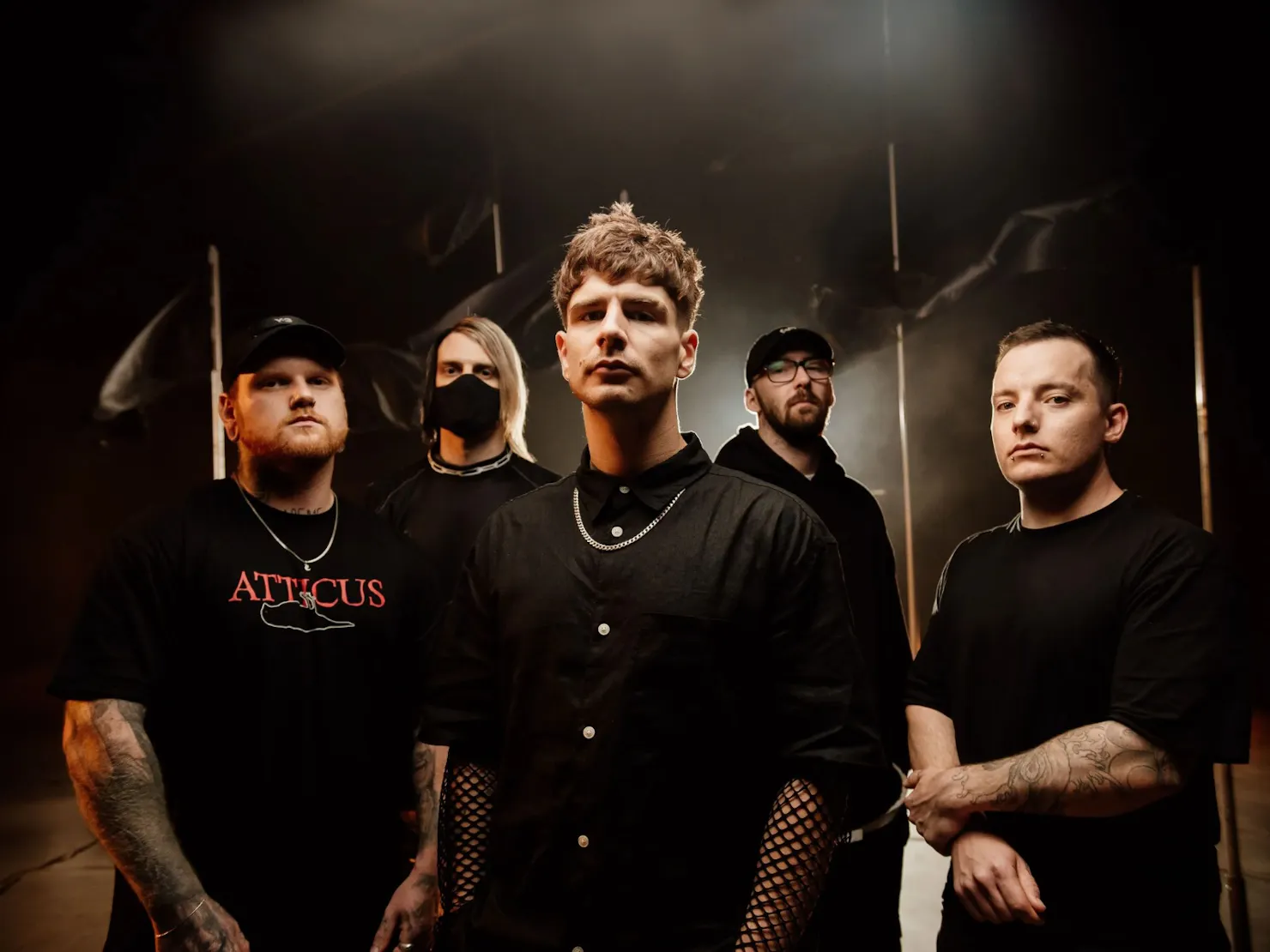 All 5 band members standing in black clothes in a dim Smokey light