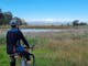 Cyclist stopped looking over the view, grass, dam distant trees, background of mountains, blue sky