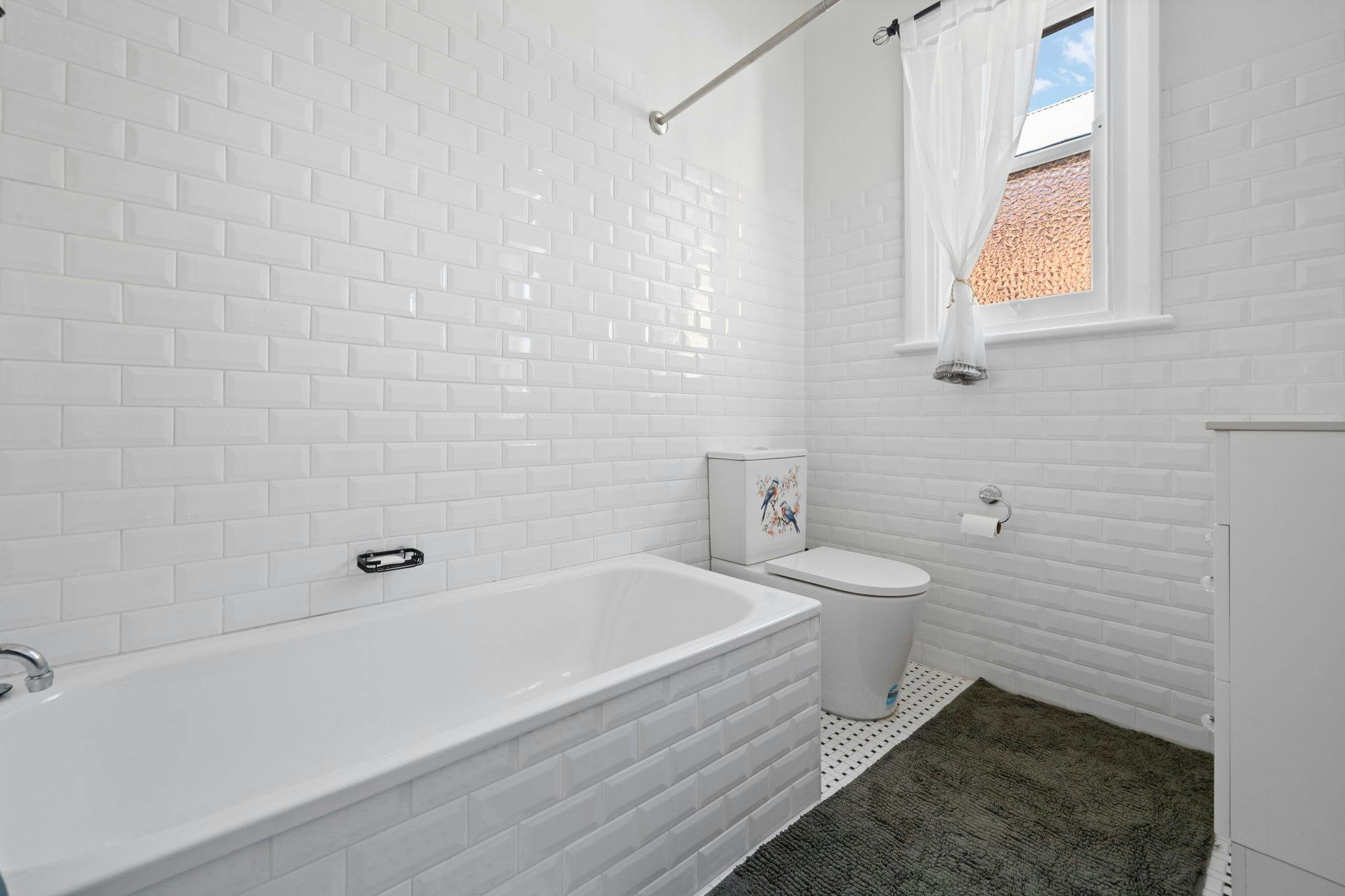 バスタブ、シャワーカーテン、小窓、トイレ、化粧台を備えた白いバスルーム。