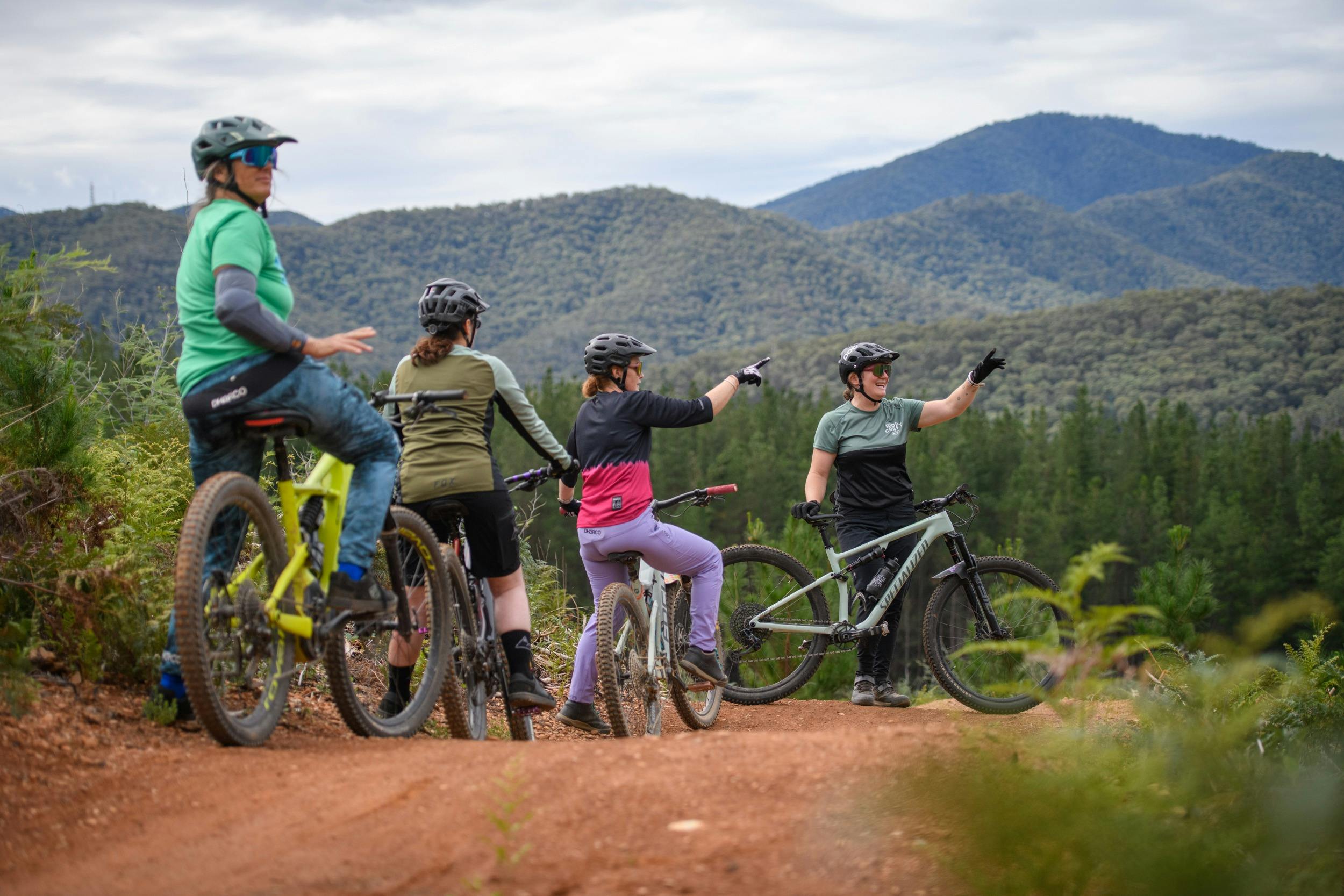 A group of female mountain bikers sit on their bikes while a guide points out a point of interest