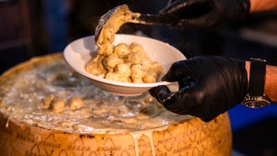 Someone serving gnocchi with cheese from a big cheese wheel