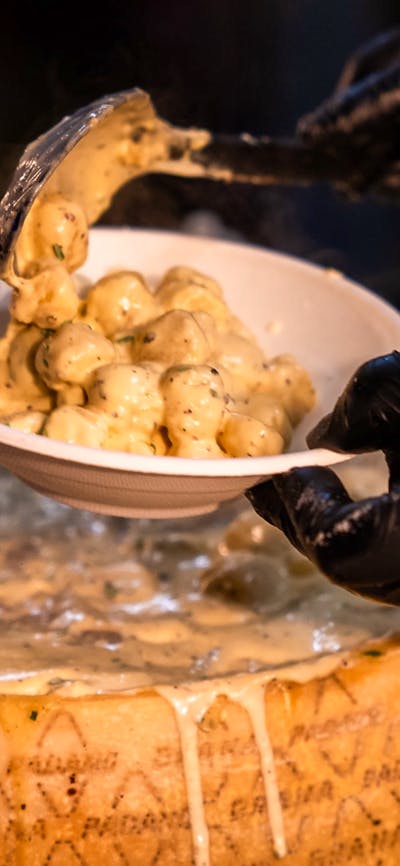 Someone serving gnocchi with cheese from a big cheese wheel