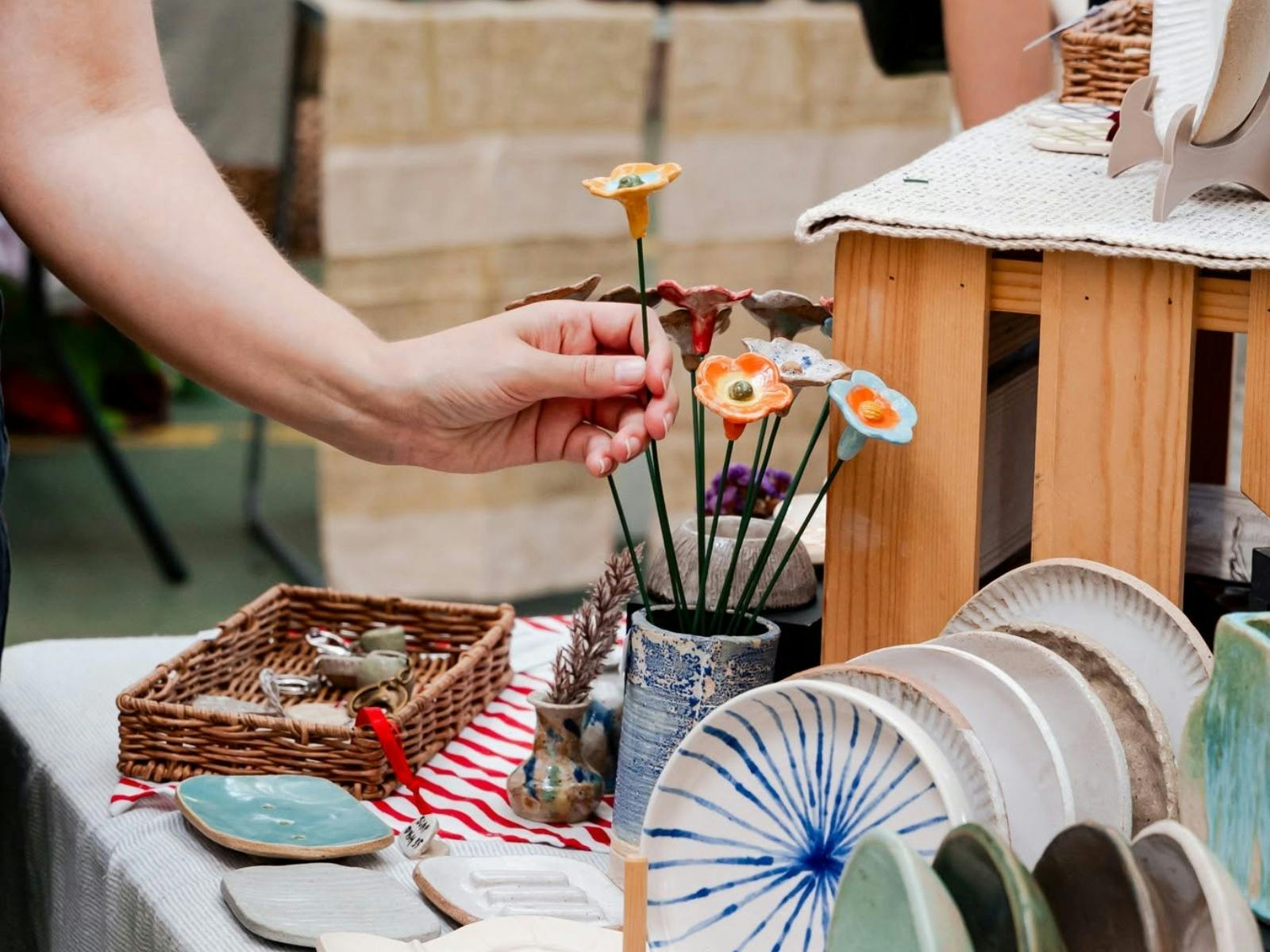 A close up of a hand picking up a ceramic flower from a ceramic vase on a market stall