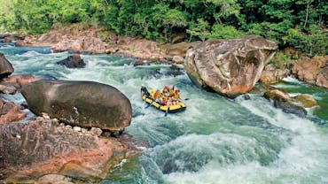 Wide shot of a rafting boat surrounded by blue water, lush rainforest and large boulders in Tully