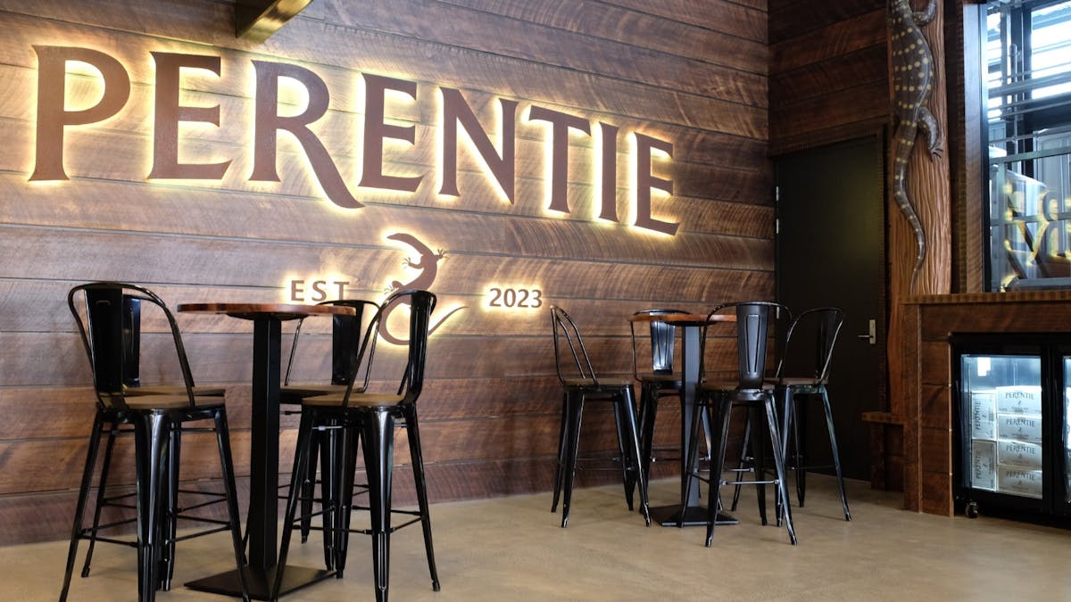 wooden paneling with a lit-up sign of the Perentie logo, with high tables and high chairs in front