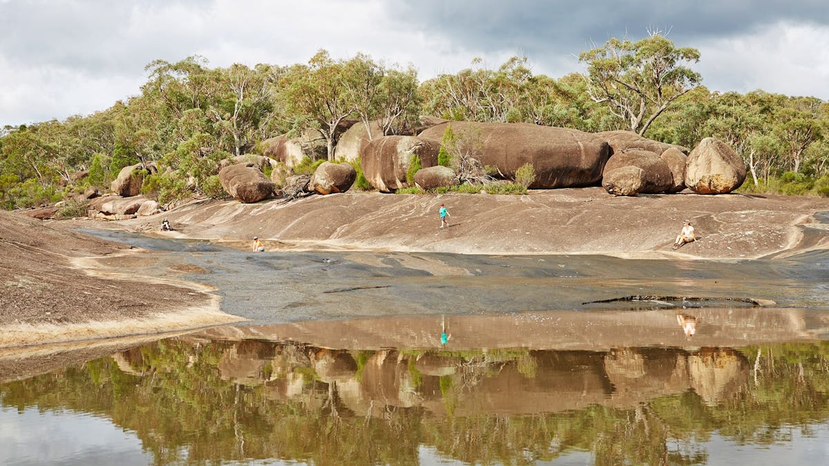 A larger rock pool surrounded by freestanding granite rock formations and native trees.