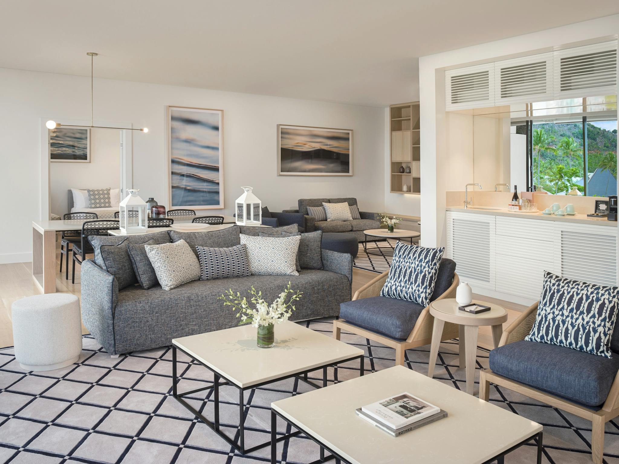 Modern living and dining space featuring blue sofas, patterned pillows, sleek tables, and large wind Modern living and dining space featuring blue sofas, patterned pillows, sleek tables, and large wind