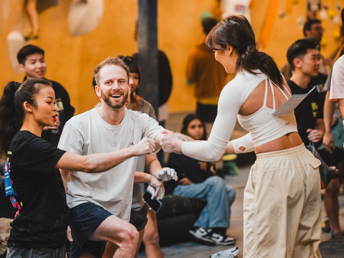 A trio of strangers smiling & "fist-bump" which is a recognition of completing or "topping" a climb