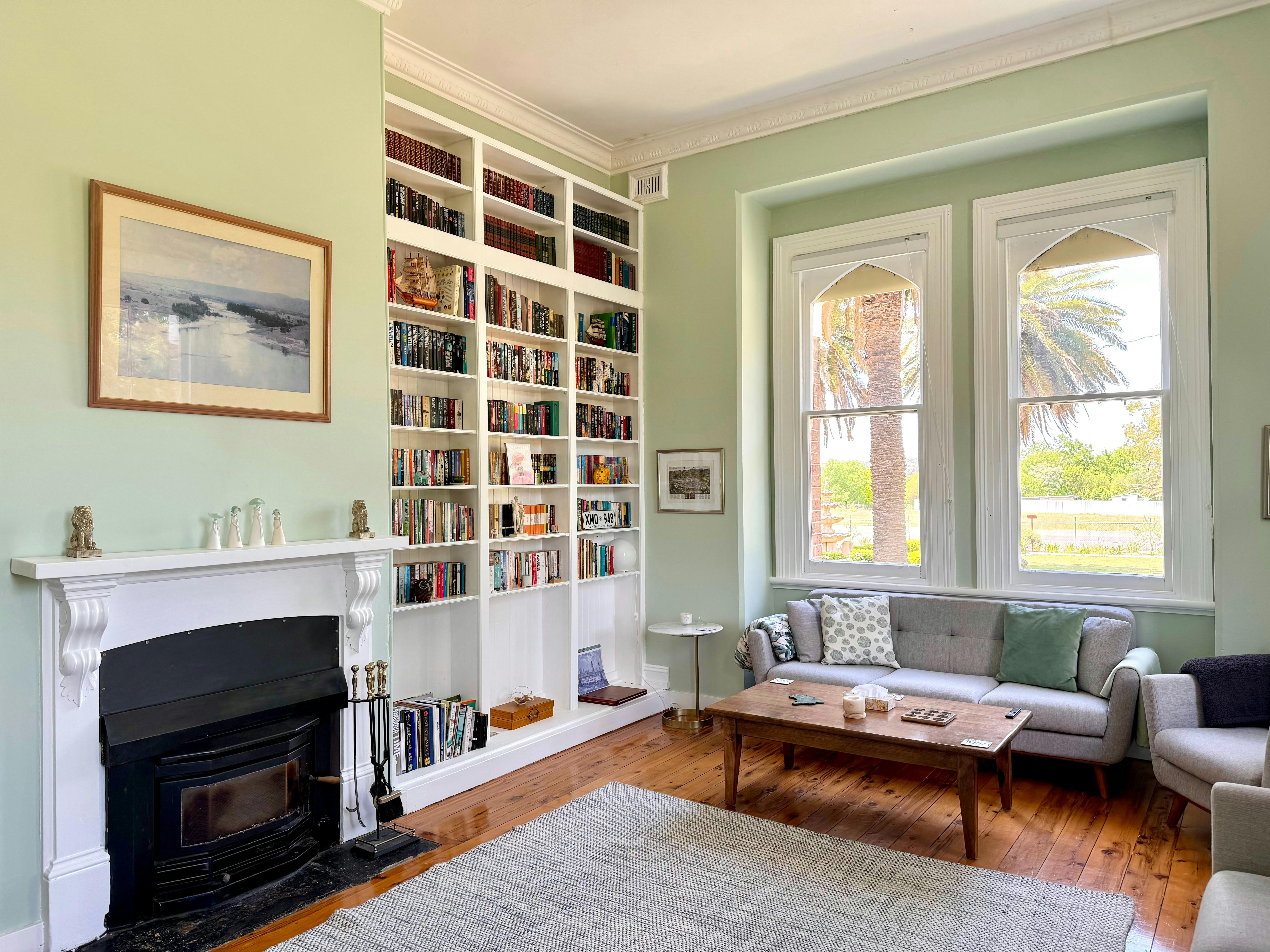 Light green coloured living room with grand fireplace and gothic arched windows.