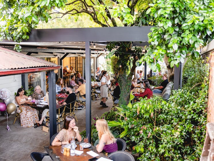 Outdoor dining area with vergola awning and lush green trees and plants