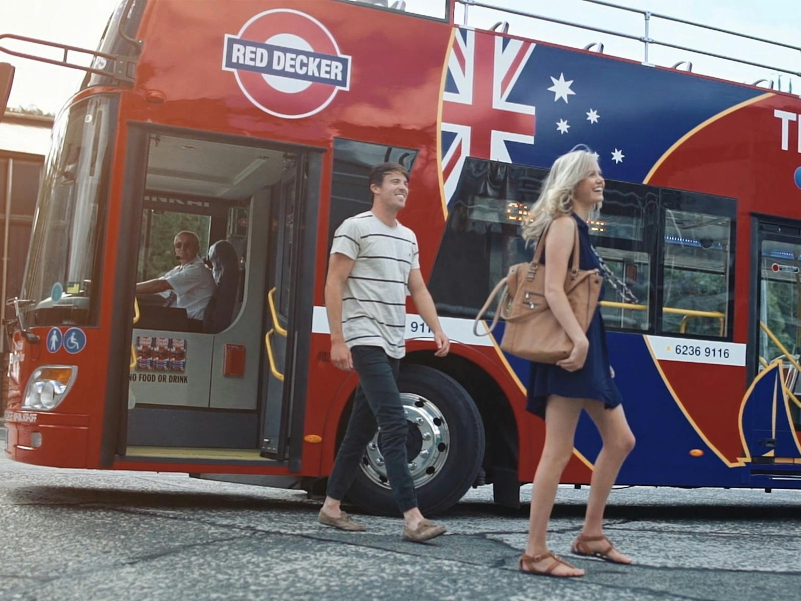 A young couple hop-off a double-decker bus.