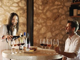 Smiling female staff member pouring wine for a guest at the Cape Jaffa Wines Cellar Door, with a ful