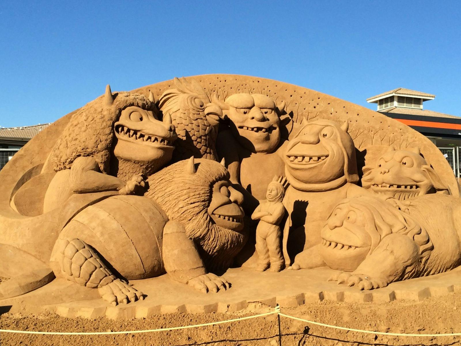 Sand sculpture of fantasy monsters surrounding a small child figure.