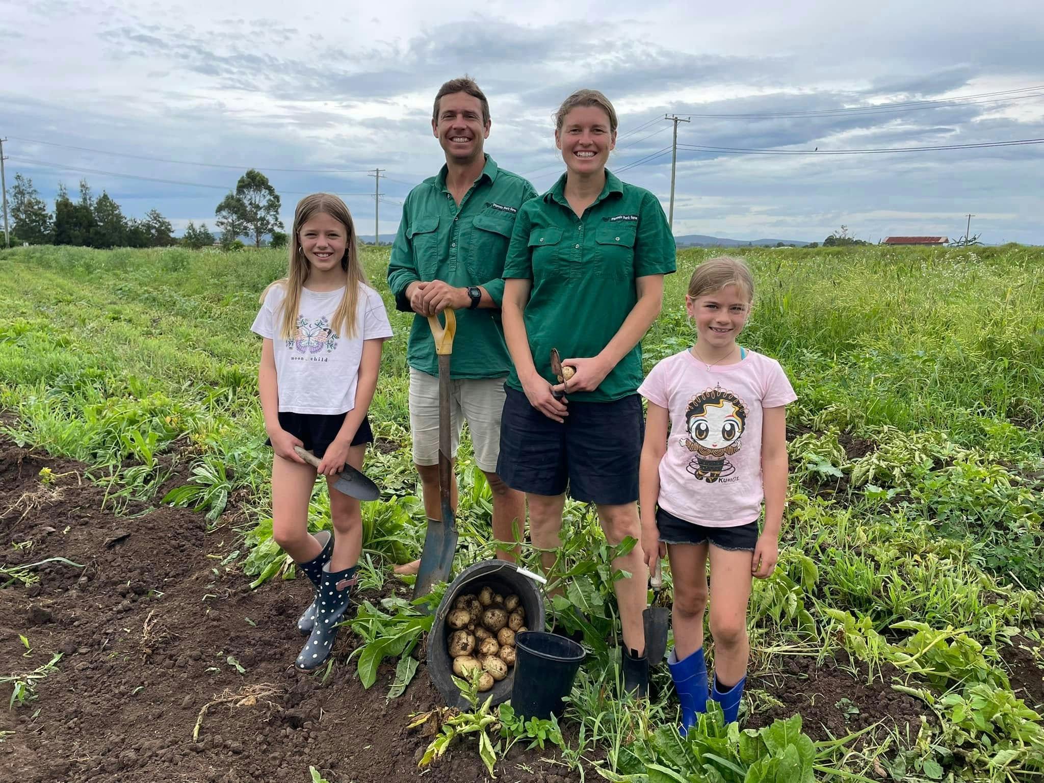 Farmer Jesse & Carly with 2 children in front of a bucket of potatoes that have just been harvested