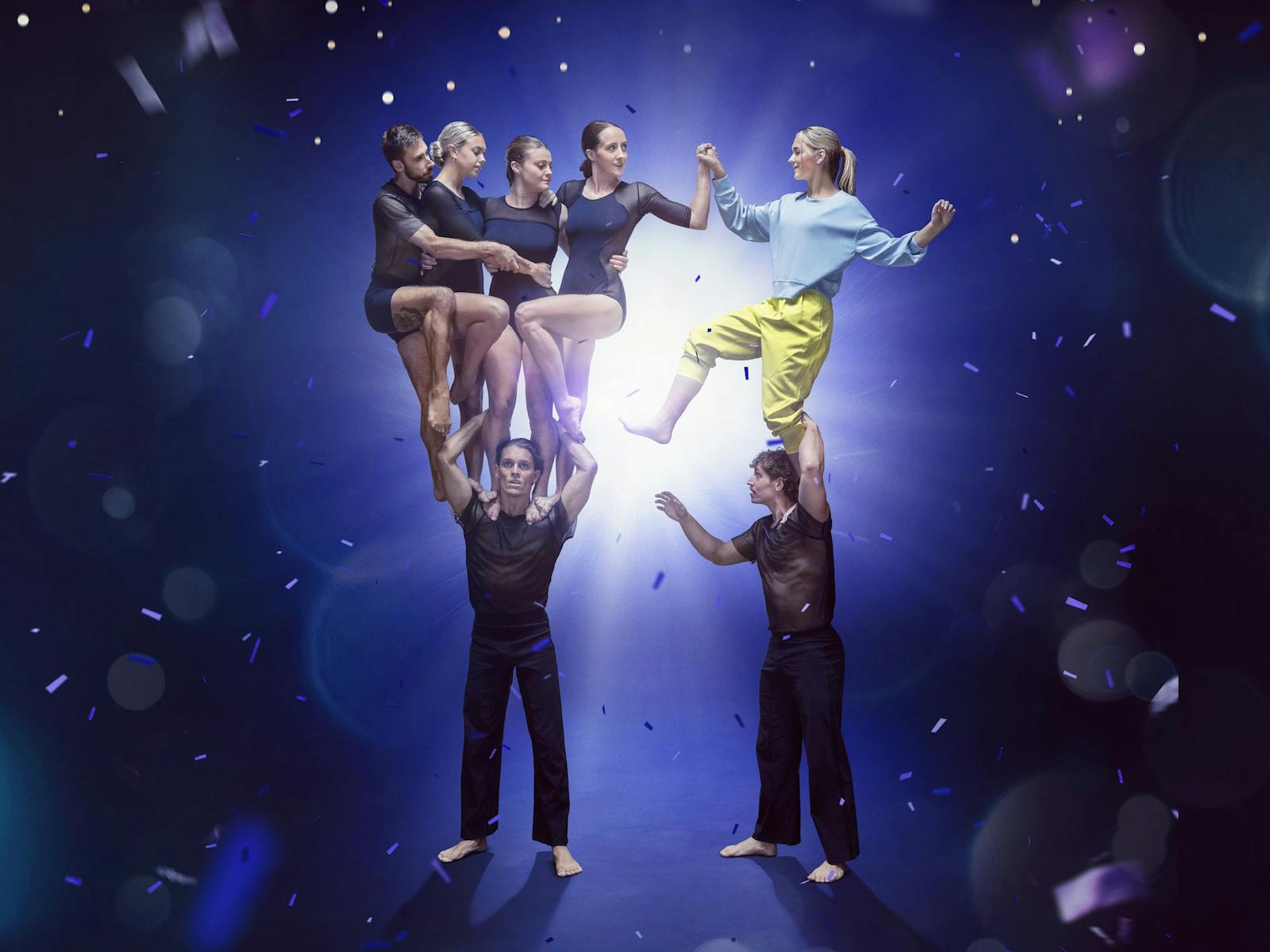 Performers standing on top of each other surrounded by a blue sparkly background. Performers standing on top of each other surrounded by a blue sparkly background.
