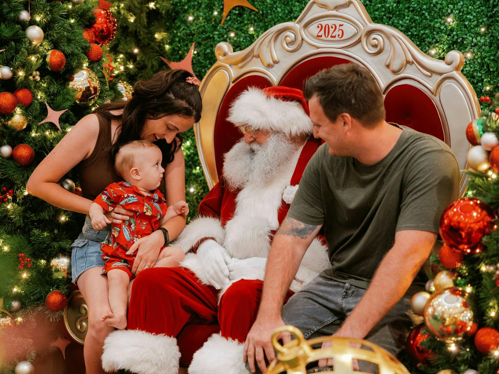 Family with a baby dressed in matching Christmas outfit sitting next to Santa Claus