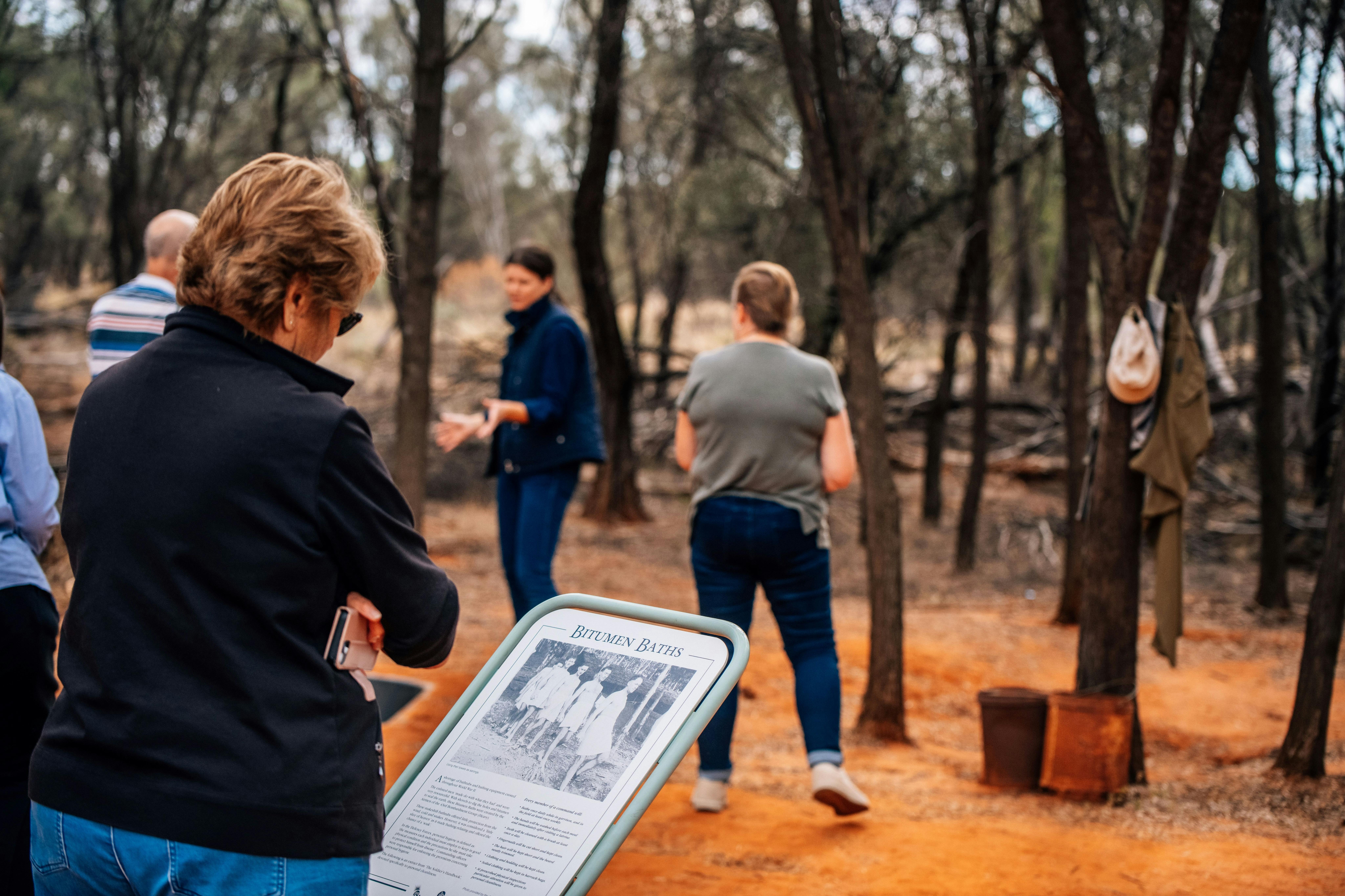 a woman in the foreground reading an info sign while the guide speaks in the background