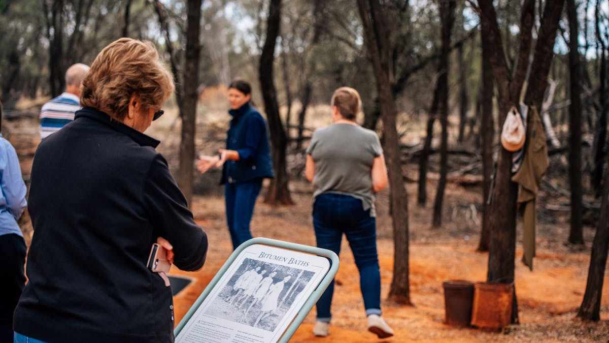 a woman in the foreground reading an info sign while the guide speaks in the background