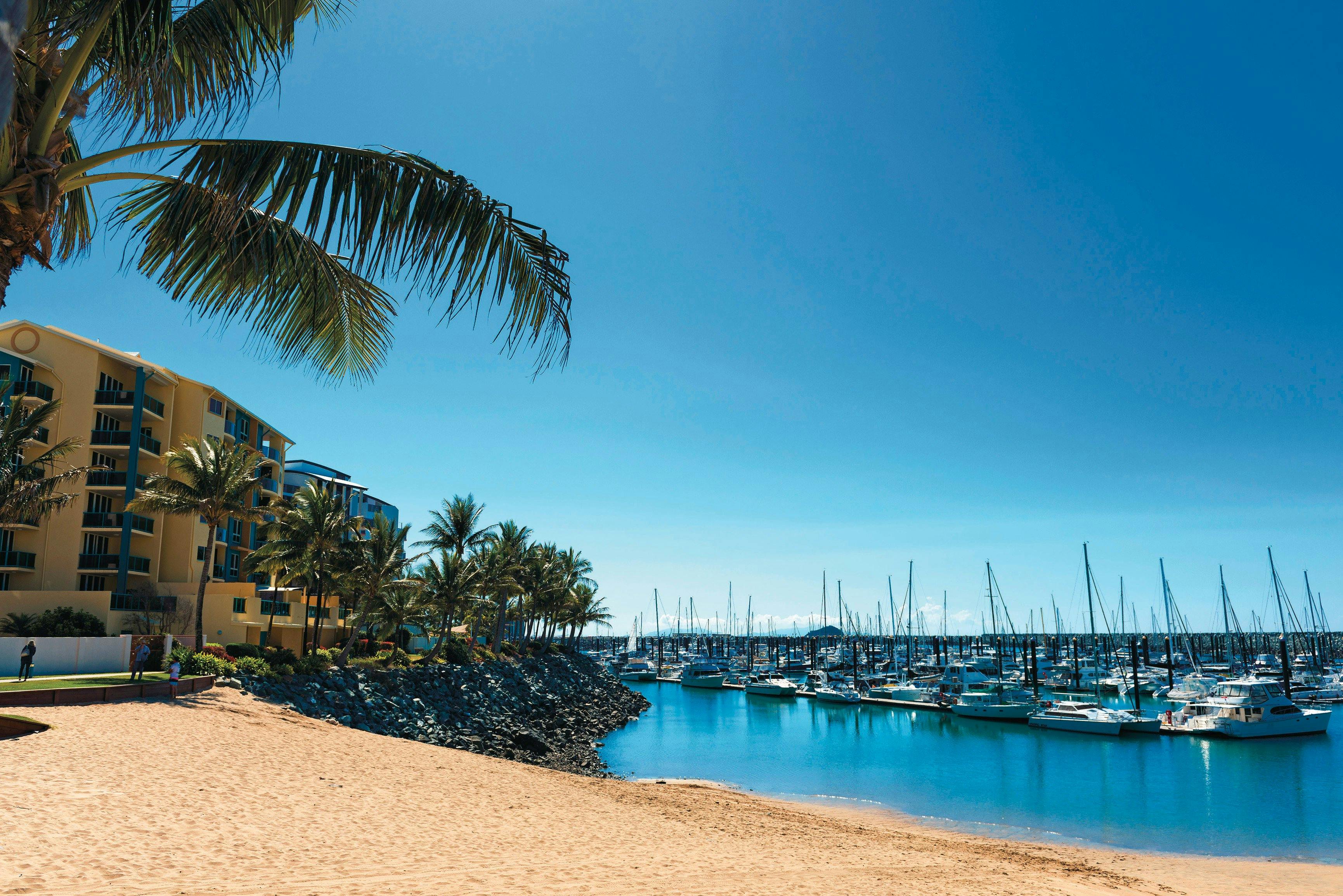 Boats tied up at the Marina from the beach buildings in the background and palm tree, sun is shining