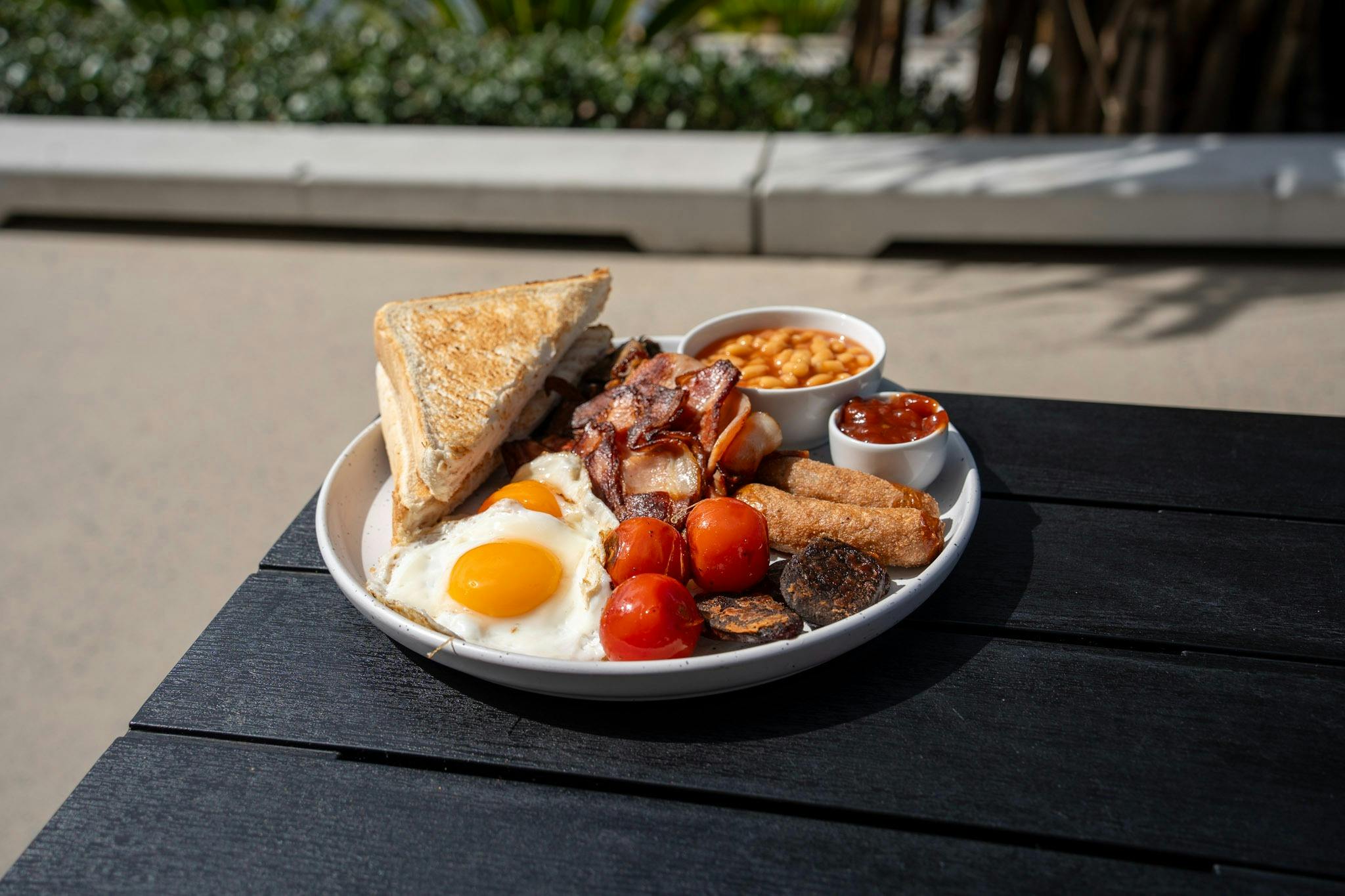 Breakfast plate with eggs, bacon, toast, beans, tomatoes and potato rösti.