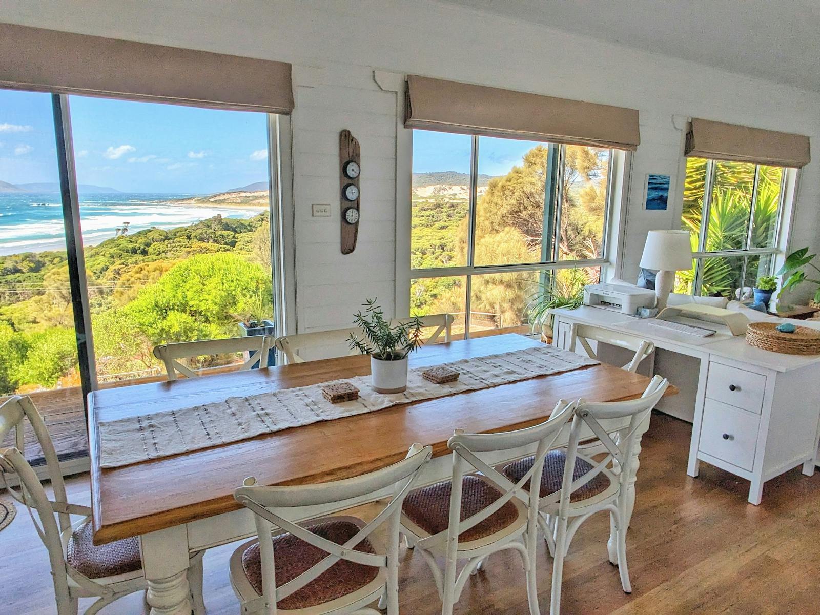 8 seater dining table with desk behind. Large windows look out to view of ocean.
