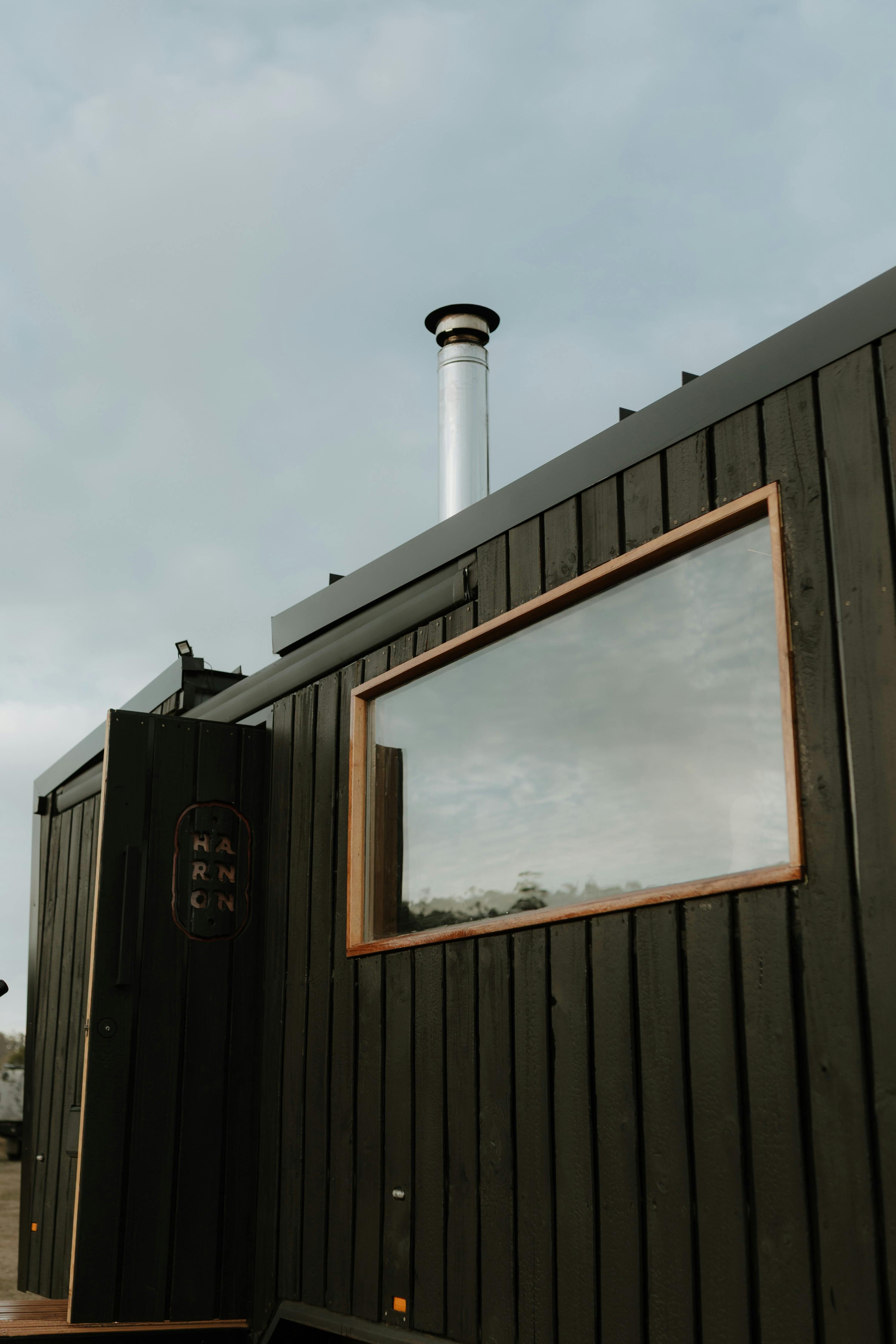 Exterior of a black timber sauna with a large picture window.