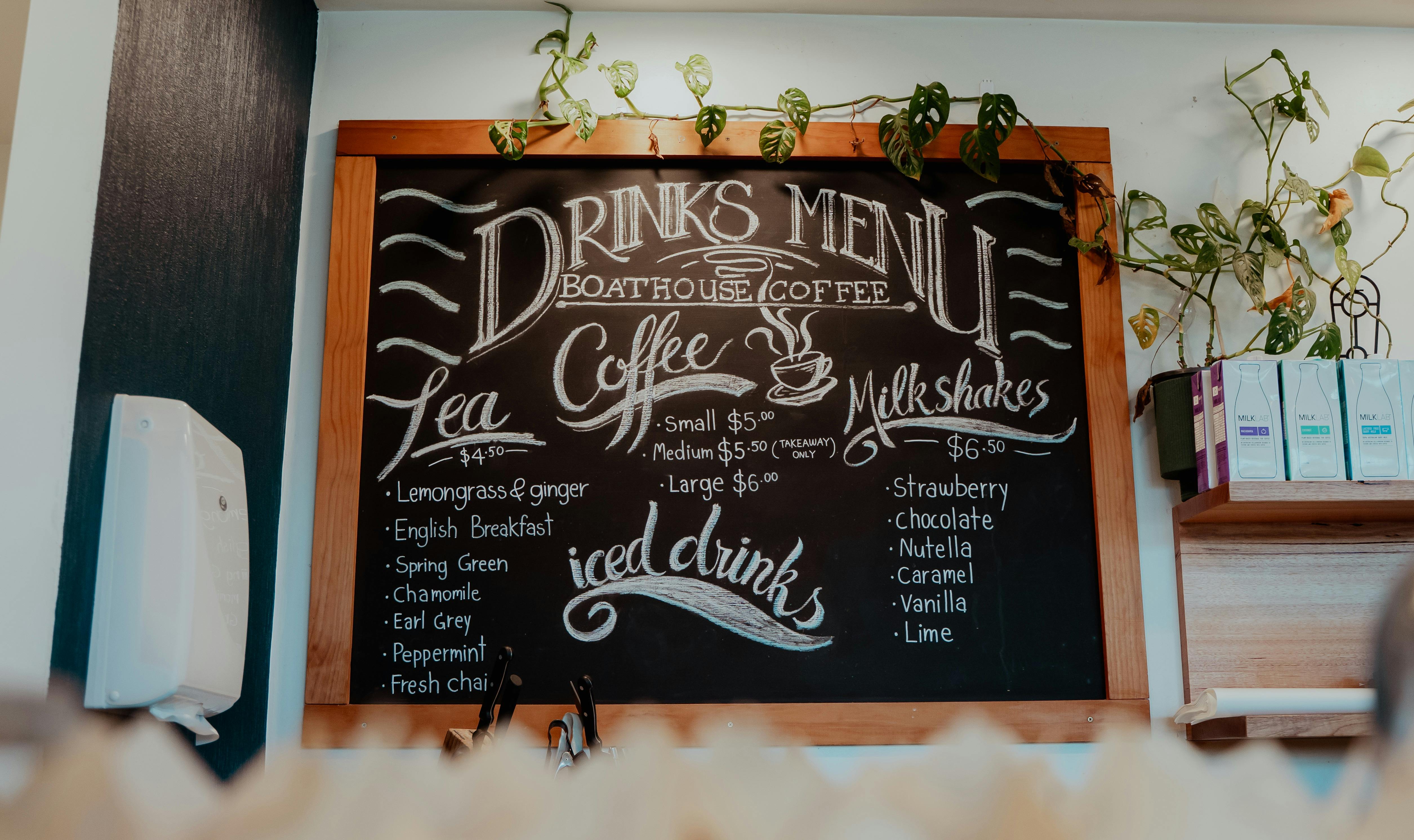 A chalkboard style menu on a wall with cursive decorative script and coffee and snacks