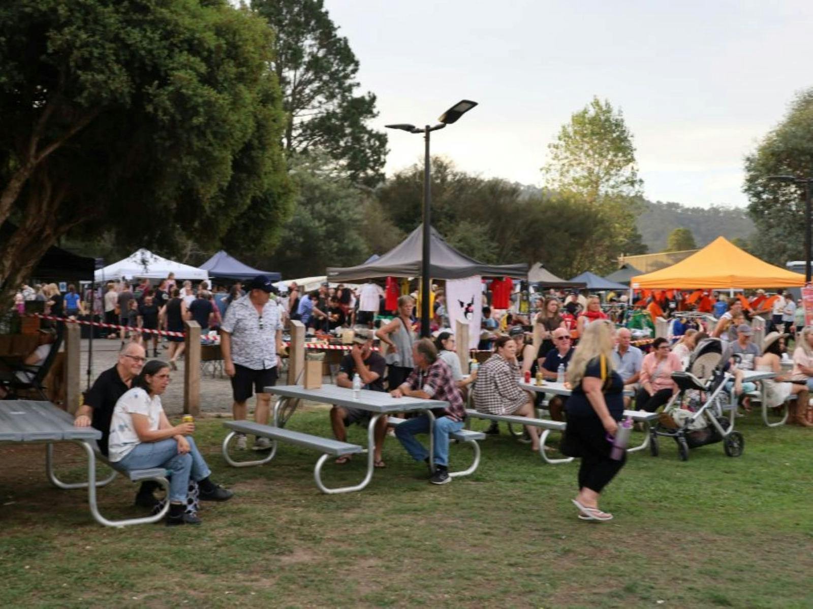 people sitting on metal benches with marquees with trees in the background